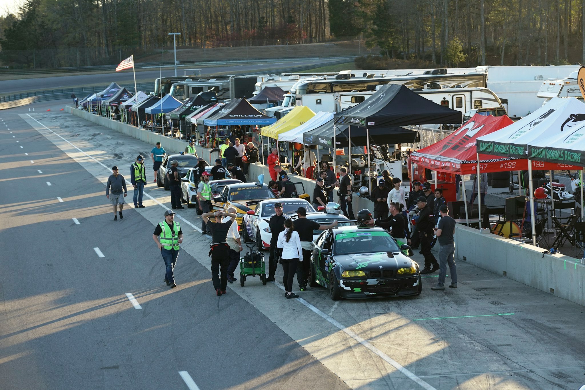 Race cars and crews lined up along pit lane at a club motorsport event